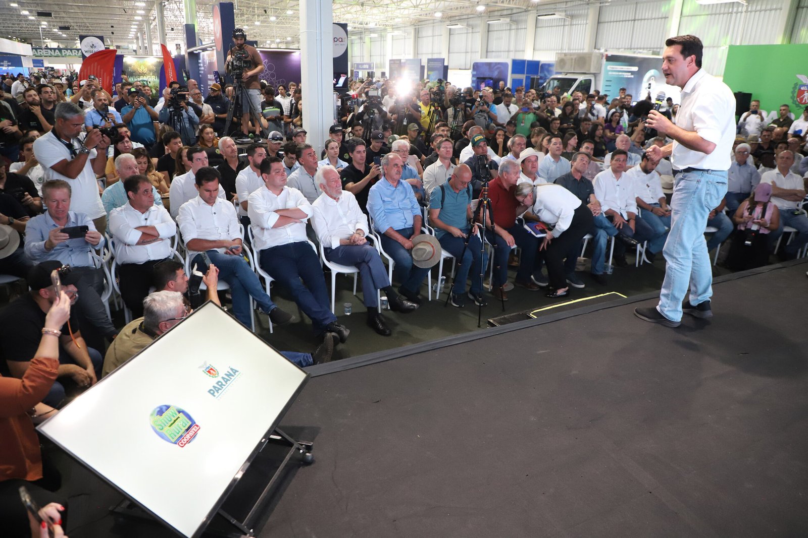 O governador Carlos Massa Ratinho Junior desembarcou em Cascavel nesta segunda-feira (09) para a abertura do Show Rural Coopavel com a caneta cheia. Aproveitando a vitrine de um dos maiores eventos do agronegócio da América Latina, o chefe do Executivo estadual anunciou um pacote de investimentos que soma quase R$ 38 milhões. Os recursos abrangem três frentes estratégicas: infraestrutura logística, educação básica e ensino técnico agrícola. O maior destaque ficou para a solução de um gargalo histórico na BR-277 e a modernização da frota de colégios que formam a mão de obra do campo. Fim do gargalo no Cascavel Velho A obra mais aguardada pela população local foi confirmada: a construção da trincheira na BR-277, que ligará os bairros Região do Lago e Cascavel Velho. O Governo do Estado vai investir R$ 21,1 milhões para acabar com um dos pontos mais críticos de mobilidade e acidentes na rodovia. A nova estrutura prevê uma passagem inferior e a duplicação do trecho, conectando a Rua Munique à Rua Waldemar Casagrande. A obra deve beneficiar diretamente mais de 65 mil moradores que hoje sofrem com congestionamentos no Trevo do Portal. “Estamos comemorando este dia de Show Rural com grandes anúncios, como a ligação entre a Cascavel Velha e a cidade moderna, superando a divisão causada pela rodovia”, afirmou Ratinho Junior. Tecnologia para a futura geração do Agro Reforçando a vocação do estado, o governador entregou R$ 6,85 milhões em equipamentos para 26 colégios agrícolas da rede estadual. A lista inclui desde tratores e carretas basculantes até drones e composteiras elétricas. O objetivo é transformar as escolas em "cooperativas-escola", onde o aluno aprende operando a mesma tecnologia de ponta que encontrará nas grandes fazendas e indústrias. “Nós transformamos os colégios agrícolas em verdadeiras cooperativas-escola. A ideia é que esses jovens saiam preparados tecnicamente, mas também com a cabeça cooperativista, que é o DNA do Paraná”, destacou o governador. Entre os itens entregues estão: 29 carretas basculantes; 30 perfuradores de solo; 13 composteiras elétricas (que transformam resíduos em adubo); 29 kits de agroindústria. Escola sustentável erguida em 7 meses Ainda na agenda em Cascavel, Ratinho Junior inaugurou a nova sede da Escola Municipal José Baldo, reconstruída com um aporte de R$ 10 milhões do Estado. A unidade antiga, de 50 anos, havia sido danificada por um tornado em 2023. A nova estrutura chama atenção pelo método construtivo modular (uso de placas metálicas com isolamento térmico), o que permitiu que a obra ficasse pronta em menos de sete meses. A escola conta com captação de água da chuva e energia solar, atendendo 347 alunos com conforto térmico e sustentabilidade. “Hoje, mais de 80% das crianças paranaenses estão alfabetizadas na idade certa, um índice muito acima da média nacional, o que consolida o Paraná como a melhor educação pública do Brasil”, reforçou o governador durante a entrega.